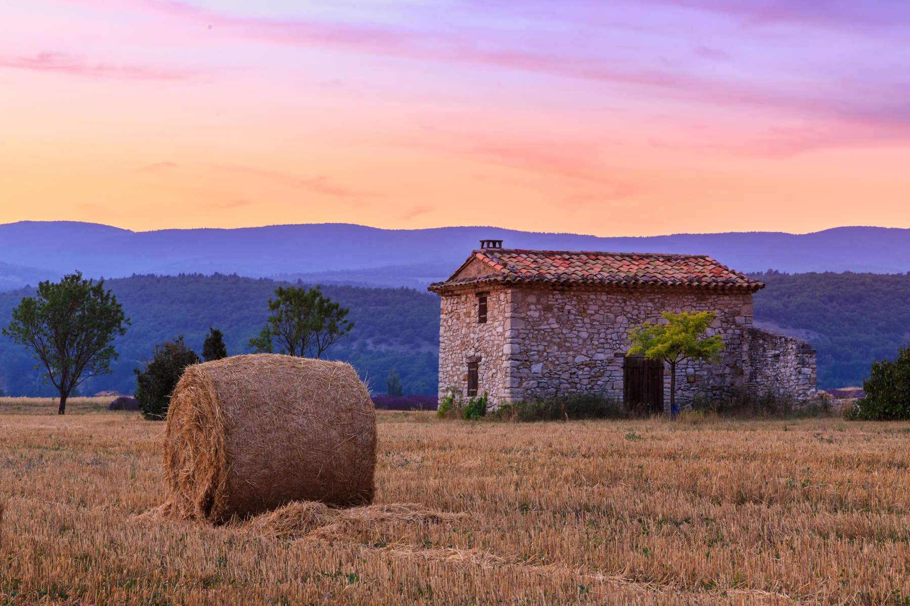 Sunset over farm field with hay bales near Sault