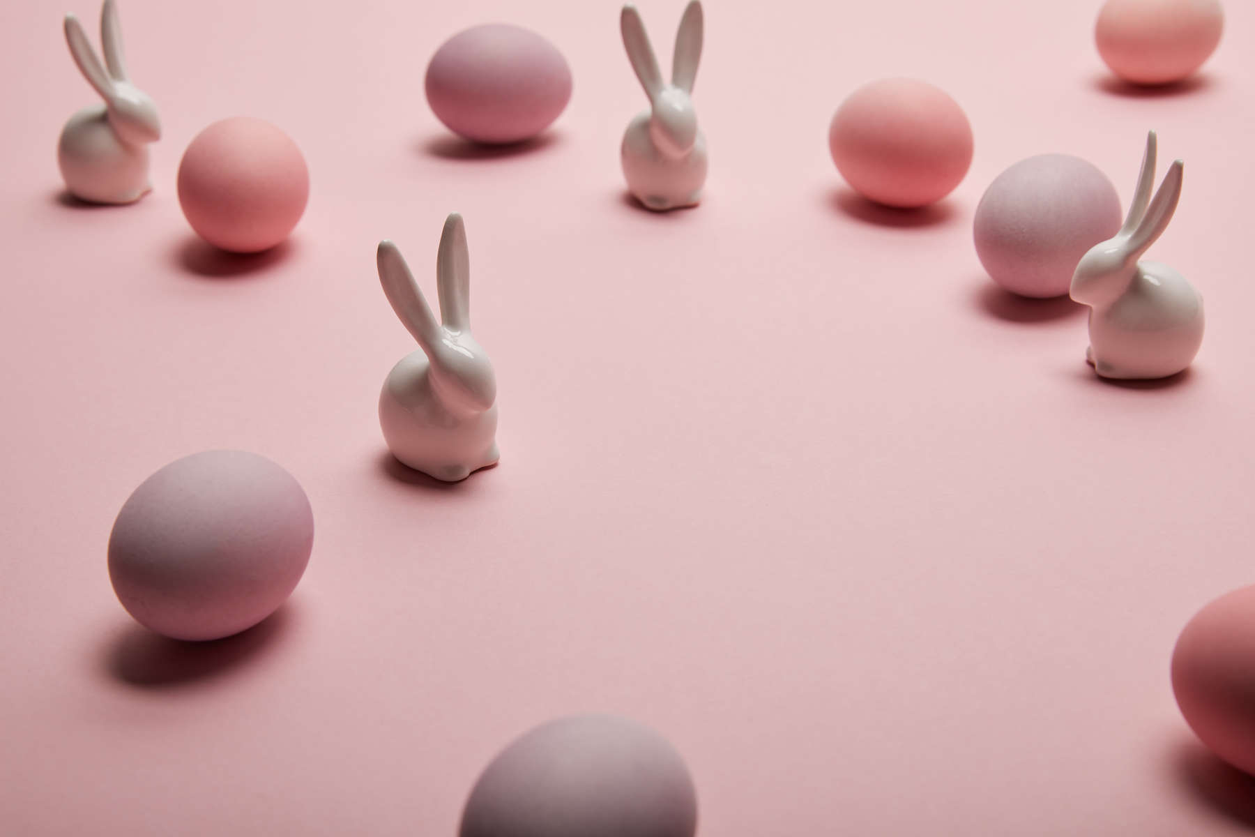 toy bunnies and painted easter eggs on pink background 