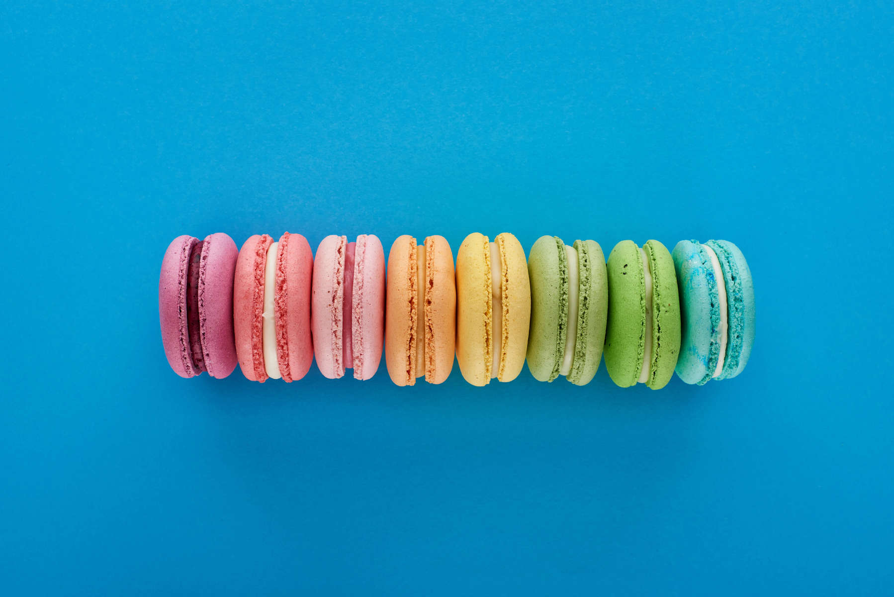 top view of colorful fresh delicious French macaroons in line on blue bright background